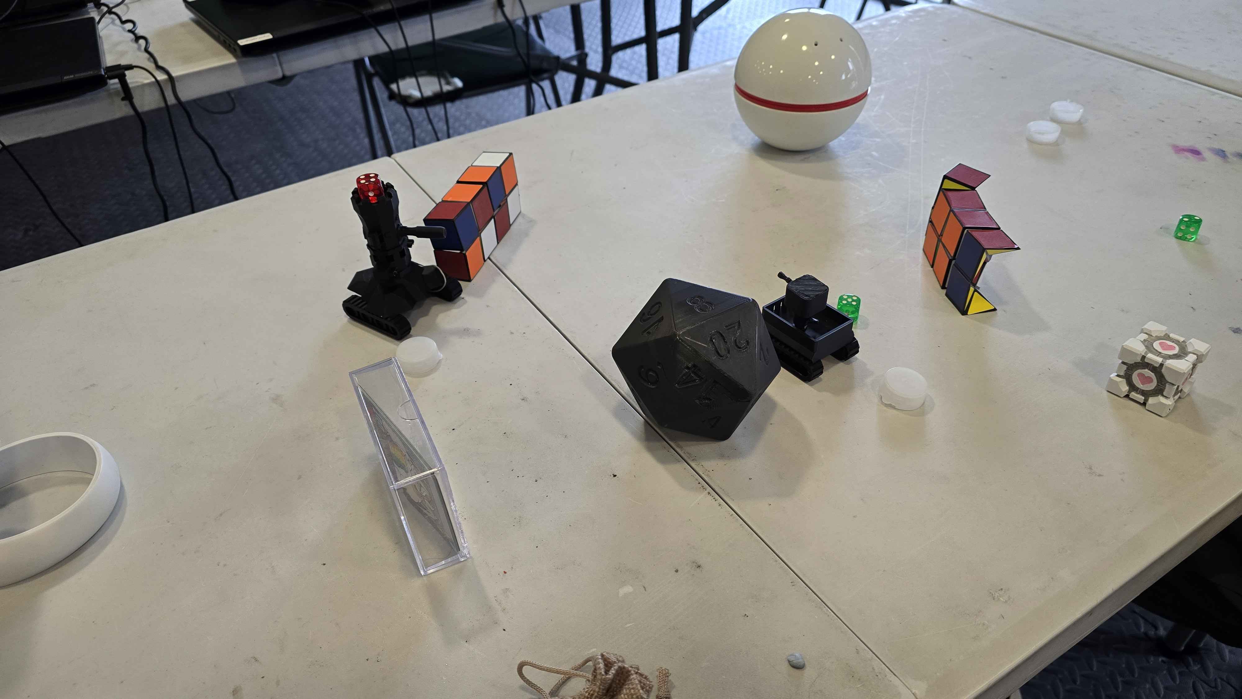 A collection of impressive 3D printed puzzles and geometric objects created by students, including Rubik's cube variations, polyhedral dice, and decorative spheres. These hands-on creations showcase the students' design skills and understanding of geometric principles through 3D modelling and printing.