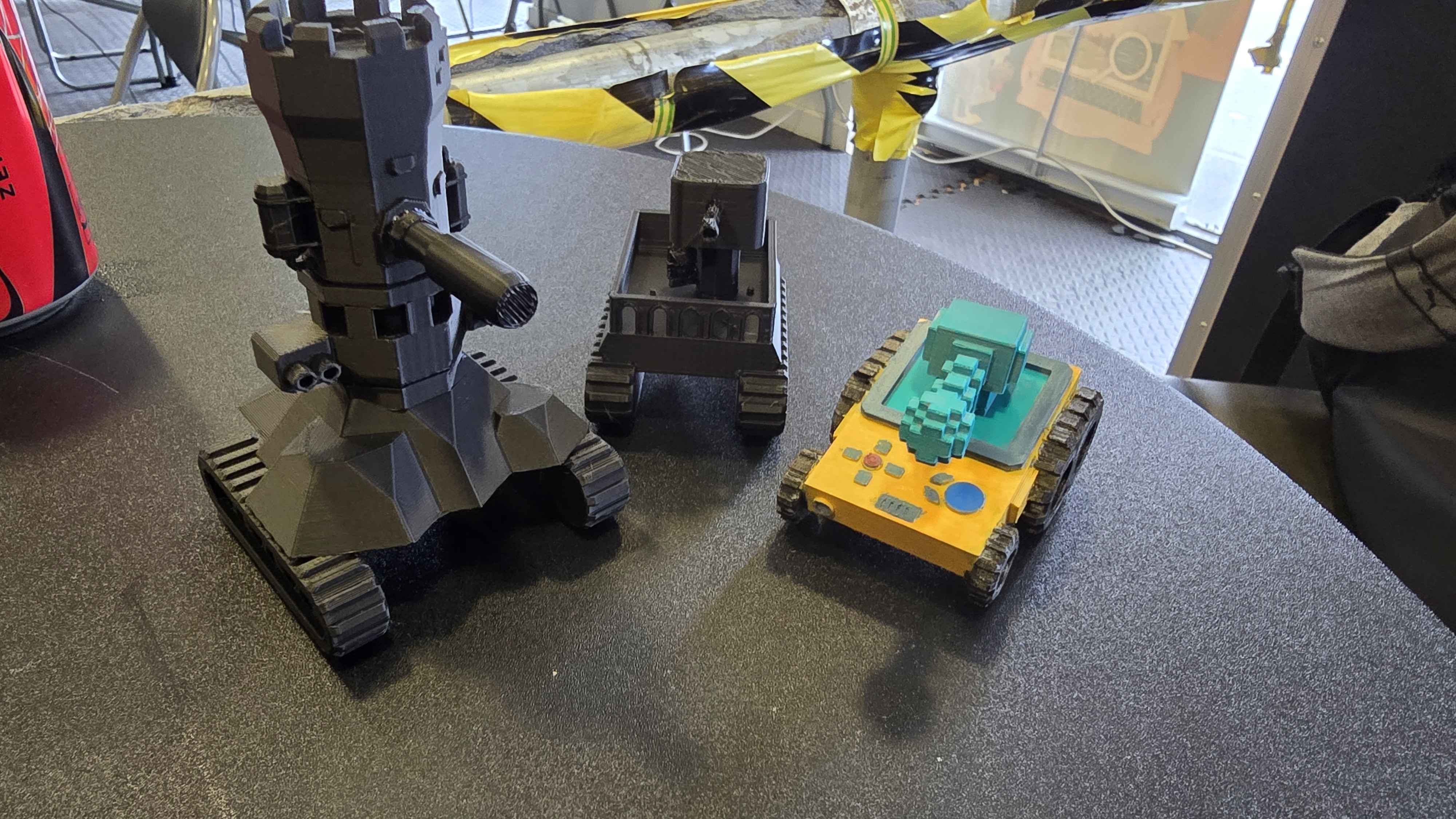Student-designed 3D printed robots featuring tank treads and creative details. Three unique robot models showcasing different designs from simple tracked bases to more complex builds with arms and tools.