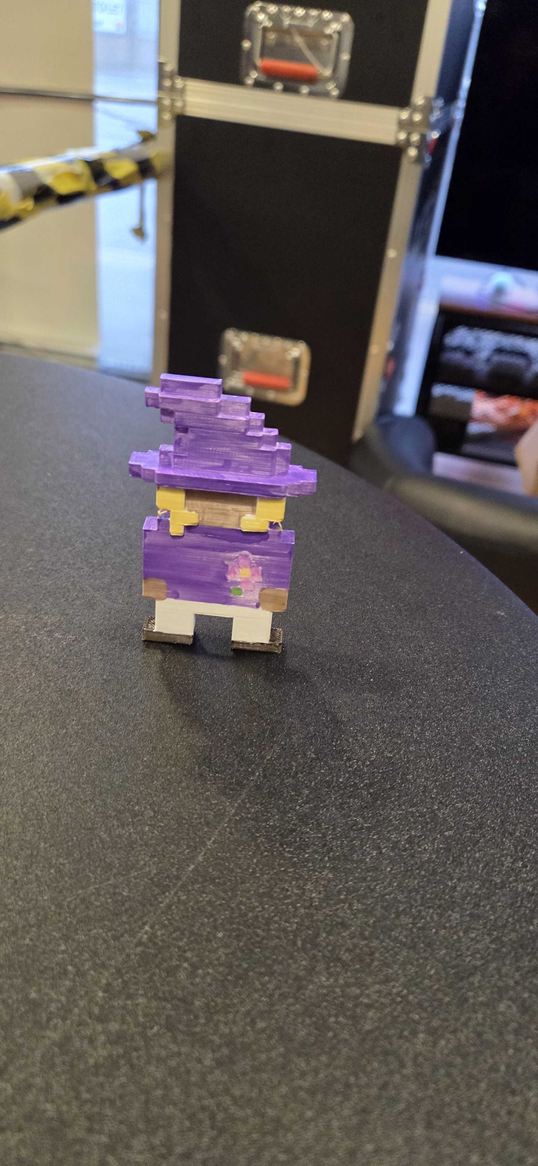 A colorful 3D printed character figure featuring purple hair and clothing with yellow accents. This pixelated design showcases creative character modeling skills brought to life through 3D printing technology.
