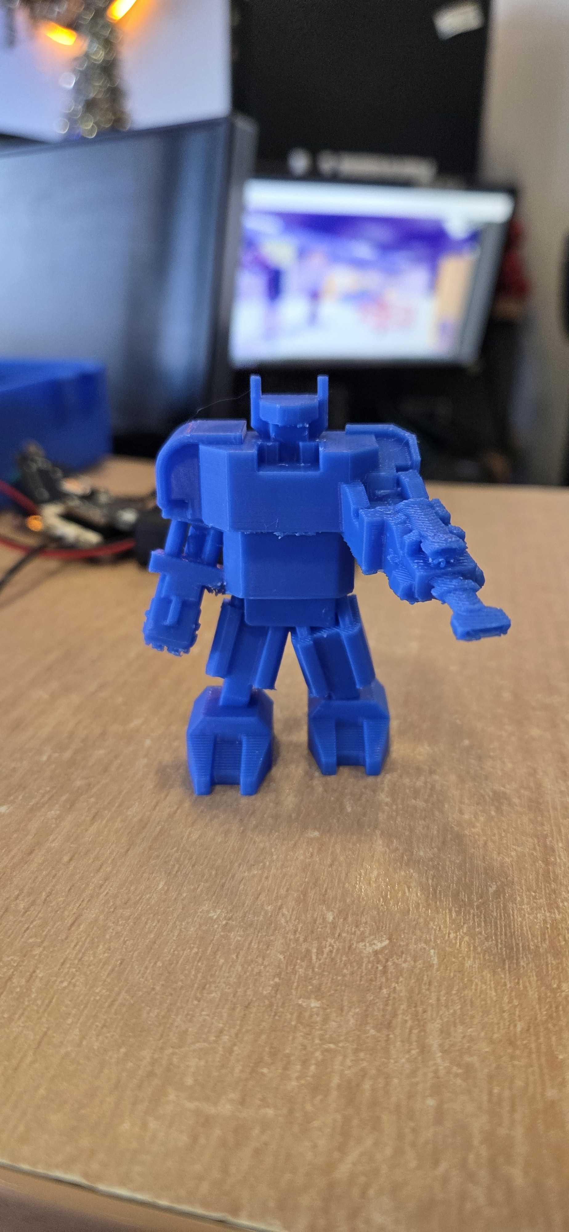 A blue robot figure brought to life through 3D printing! This blocky character design features detailed articulation with arms, legs, and weapon accessories, showcasing the student's ability to design and print a complete action figure.